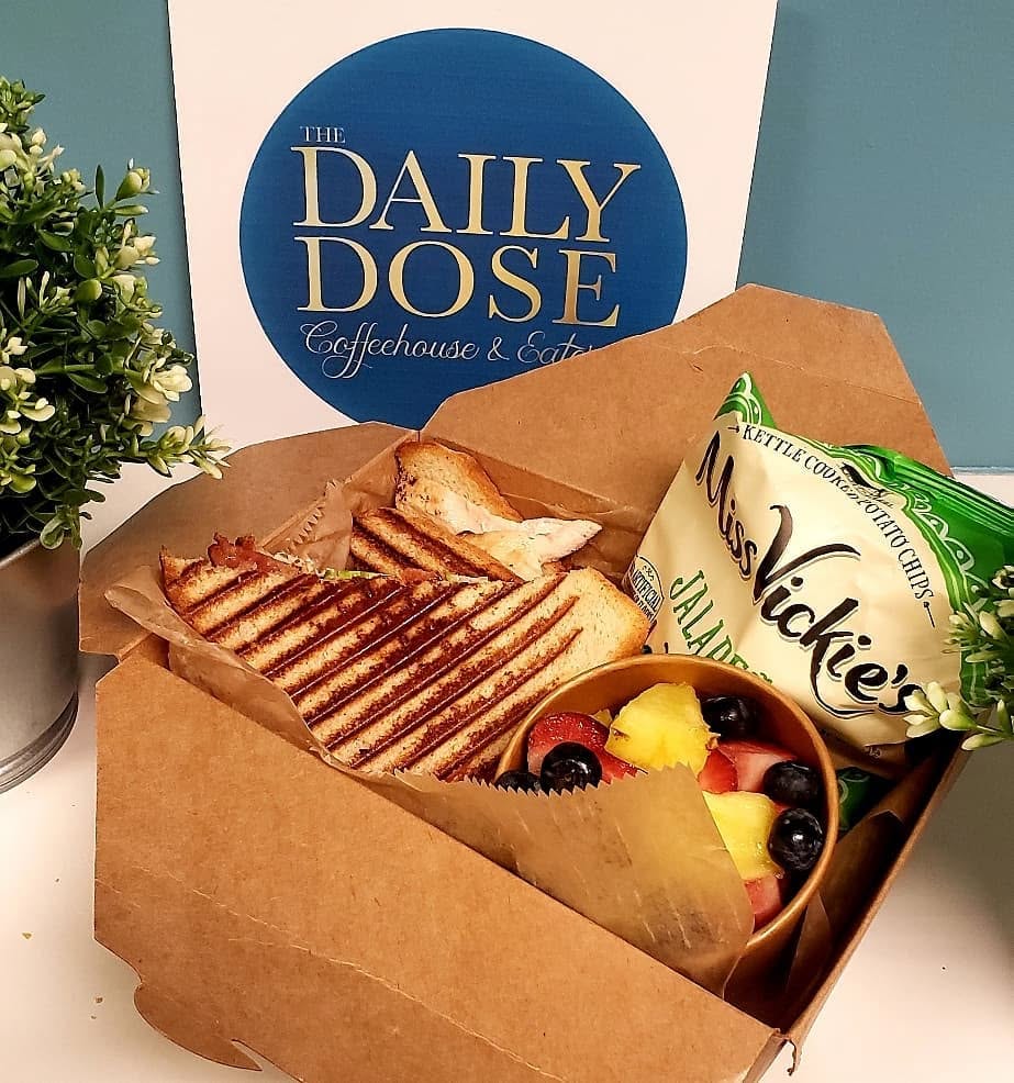 Individually boxed Daily Dose catering lunch with a grilled panini, fresh fruit cup, and kettle chips, available for group orders at both Tampa locations